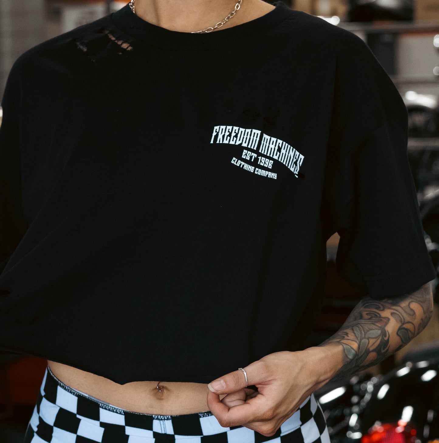 Hand distressed black crop top for women. Picture is taken in a motorcycle garage.  Front of shirt showing says "Freedom Machines" 